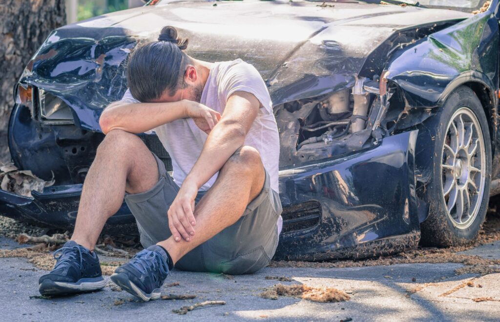 Man sitting in front of a car after being in an accident
